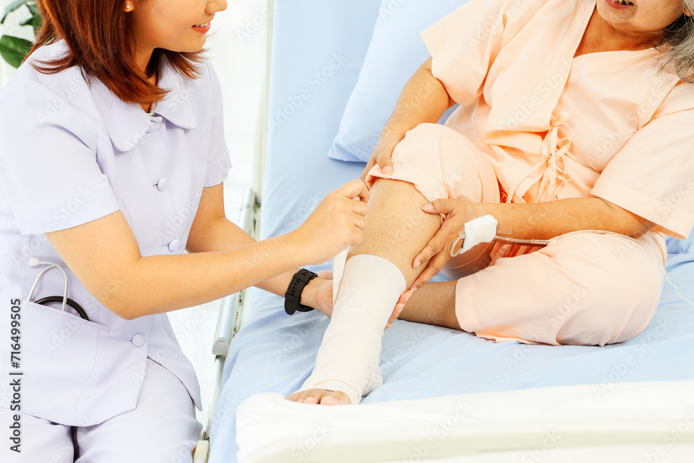 Fototapeta premium Female nurse care elderly female patient hospitalized patient with ankle pain from sprained foot Nurse uses bandage relieve pain makes patients feel good and encourages them to recover from illness.