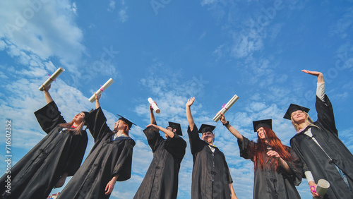 Cheerful graduates pose with raised diplomas on a sunny day. photo