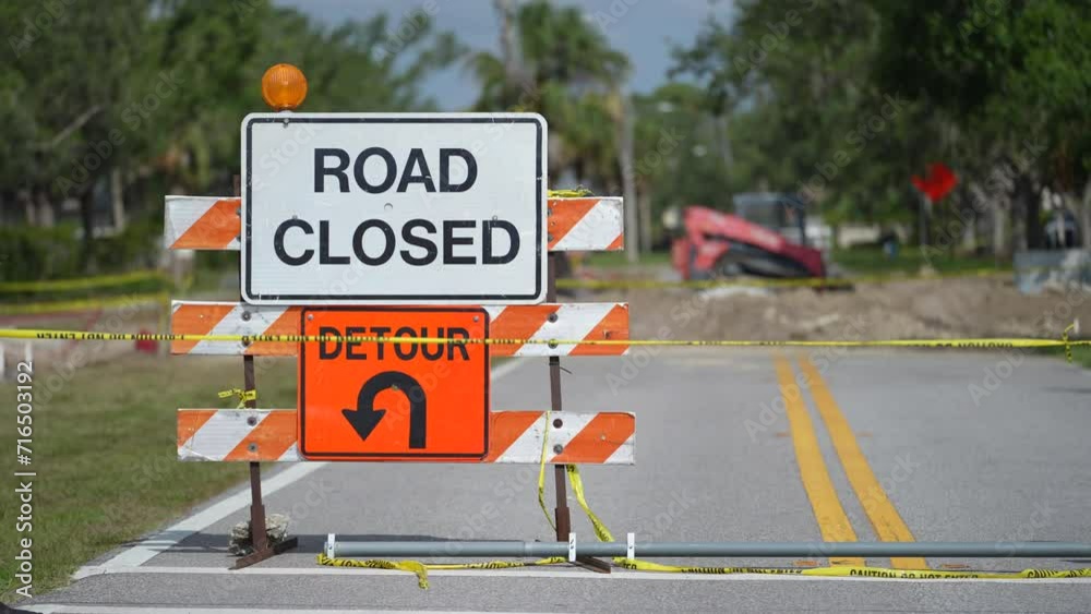 Warning roadworks sign and safety barrier on city street during maintenance repair work.