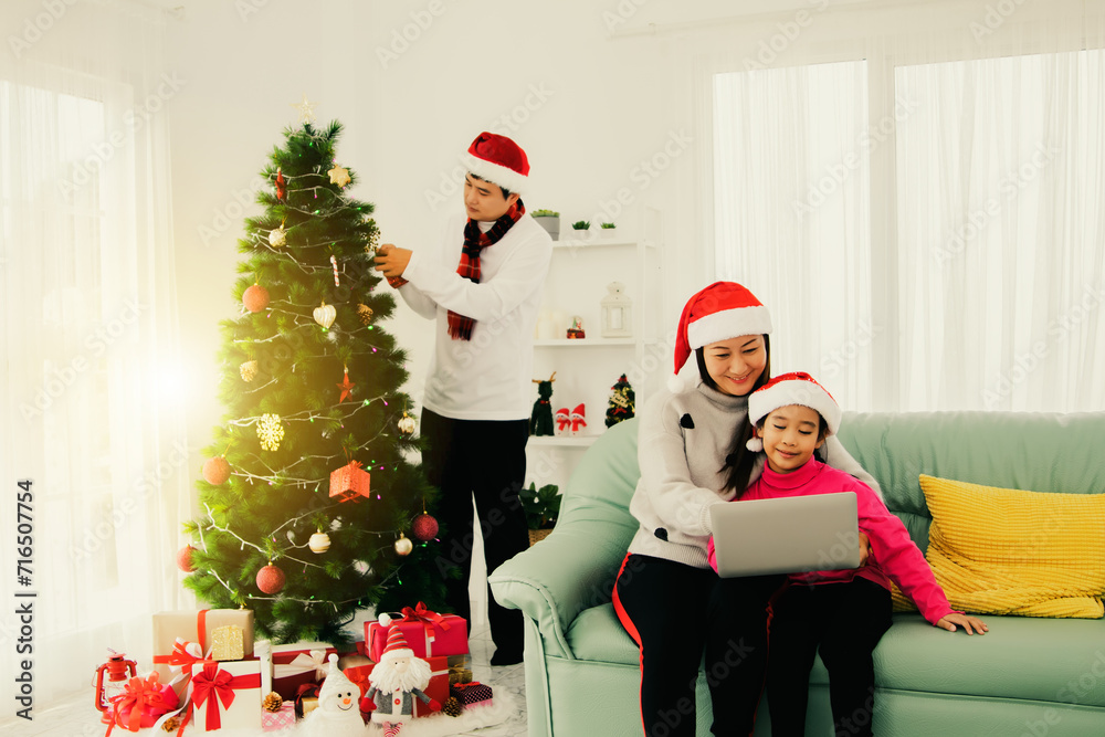 Happy family holding a Christmas party in their home : Decorate the christmas tree with beautiful gifts as father and mother and daughter sit on the sofa and relax comfortably. Happy family holding a Christmas party in their home : Decorate the christmas tree with beautiful gifts as father and mother and daughter sit on the sofa and relax comfortably.