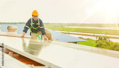 Asian male electrician engineer inspects installation of solar panels on metal roof in industrial factory sitting checking important points each solar panel gives thumbs up through quality inspection.