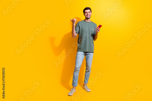 Full length photo of positive funny man dressed khaki t-shirt texting modern gadget thumb empty space isolated yellow color background