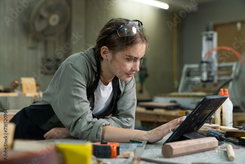 A young woman is training to be a carpenter in the workshop. smartphone and working with a laptop computer in a wood workshop. Black female carpenters contact customers by smartphone. SME orders.