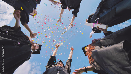 Happy graduates throwing up colorful confetti against the blue summer sky. photo