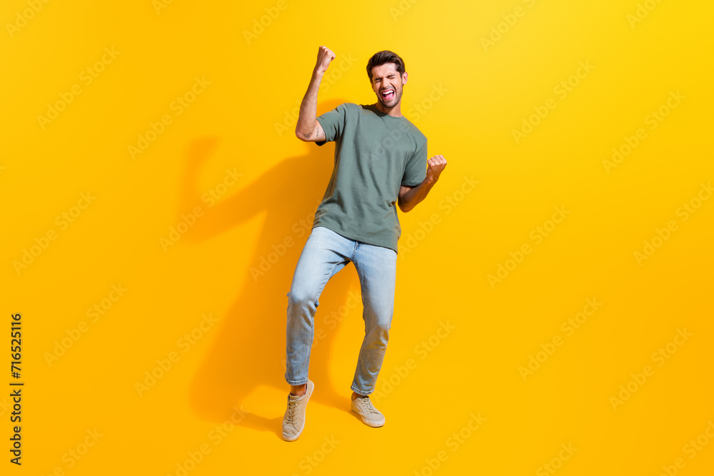 Full length photo of charming lucky man dressed khaki t-shirt shouting yes rising fists isolated yellow color background Full length photo of charming lucky man dressed khaki t-shirt shouting yes rising fists isolated yellow color background
