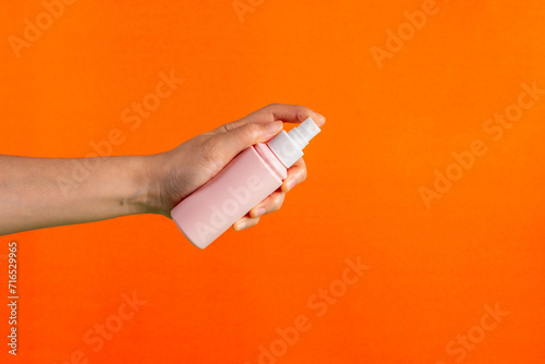 Cosmetic pink bottle. Womens cosmetic accessory and hand for makeup on orange background.