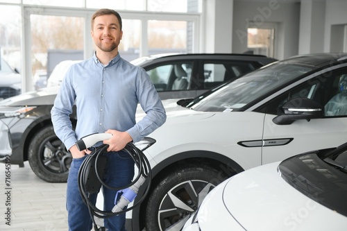 Young man, selling electric cars in the showroom. Concept of buying eco-friendly car for family © Serhii
