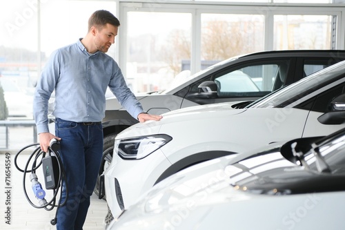 Young man buying first electric car in the showroom. Eco car sale concept