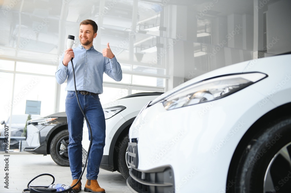 Concept of buying electric vehicle. Handsome business man stands near electric car at dealership Concept of buying electric vehicle. Handsome business man stands near electric car at dealership