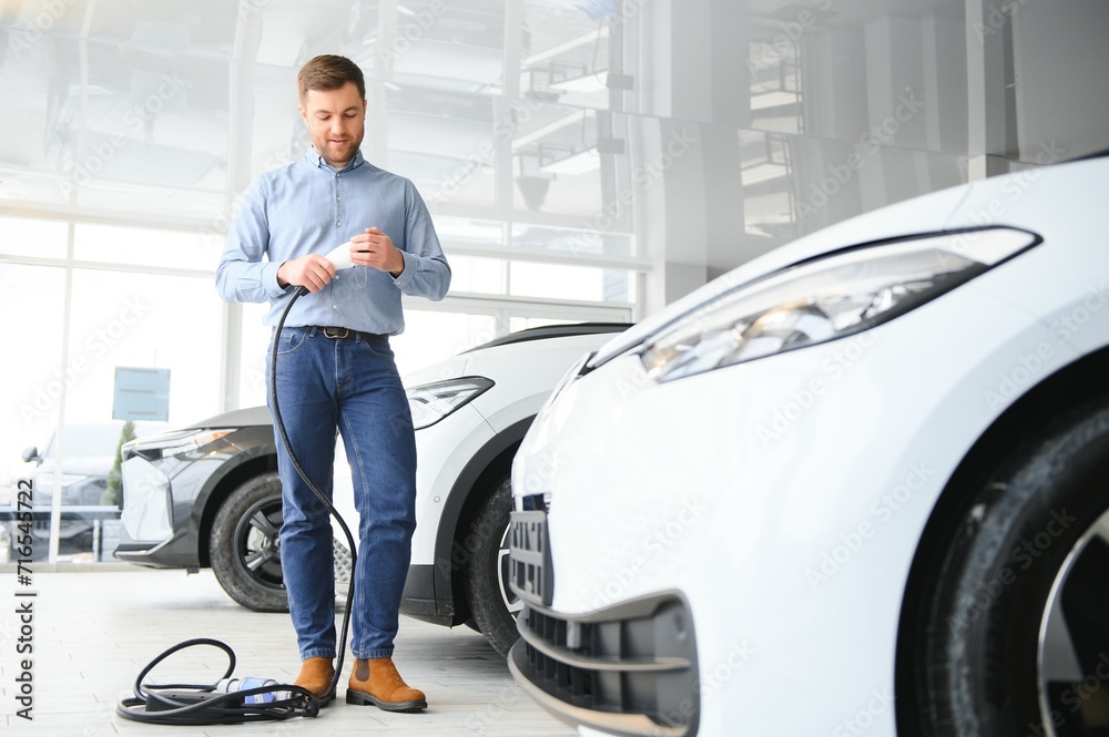 Young man buying first electric car in the showroom. Eco car sale concept Young man buying first electric car in the showroom. Eco car sale concept