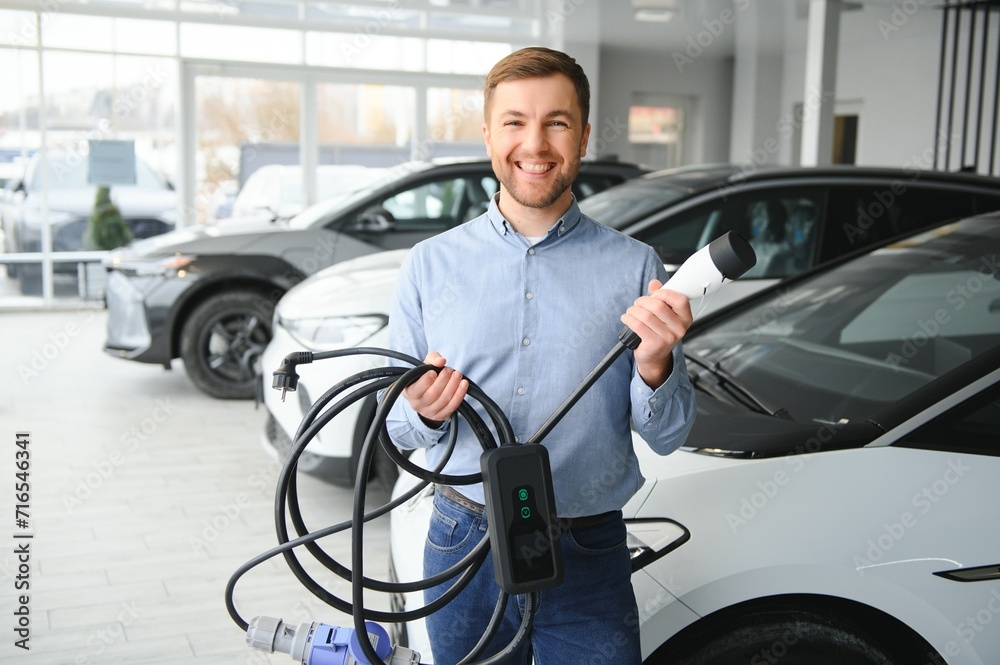 A happy man chooses a new electric car at a car dealership. The concept of buying an ecological car