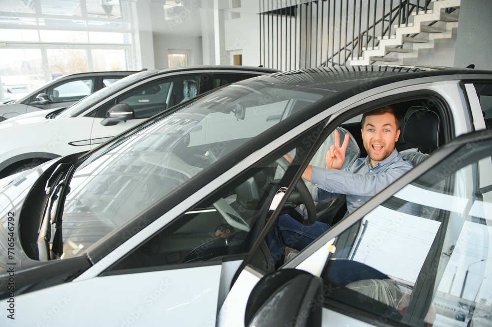 Young man, selling electric cars in the showroom. Concept of buying eco-friendly car for family