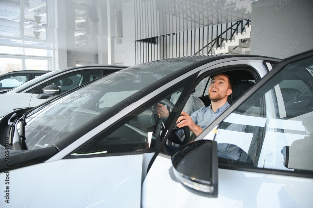Young man, selling electric cars in the showroom. Concept of buying eco-friendly car for family