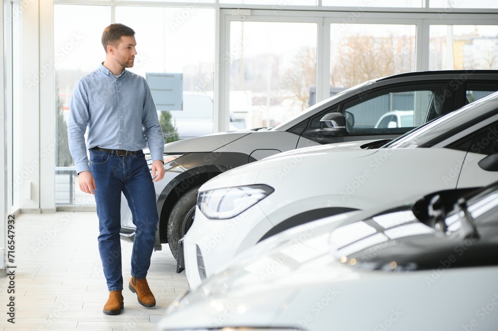 Concept of buying electric vehicle. Handsome business man stands near electric car at dealership Concept of buying electric vehicle. Handsome business man stands near electric car at dealership