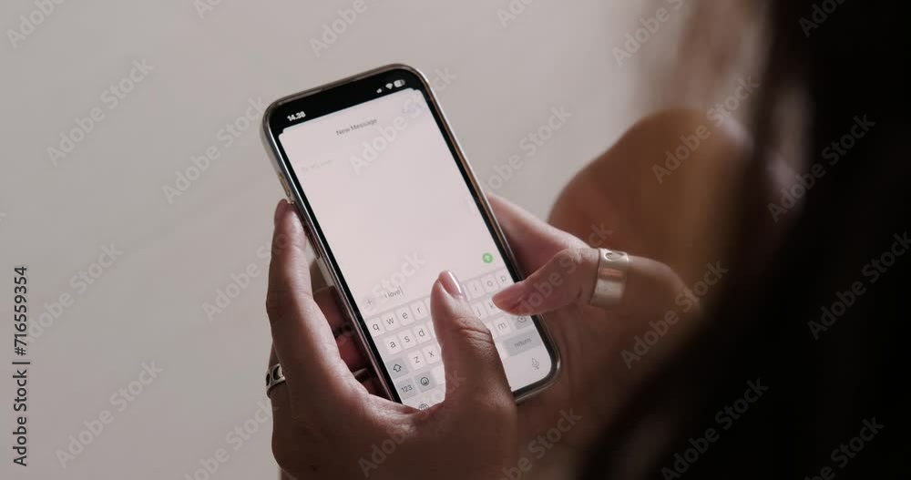 A close-up of the hands of a young woman who is typing a message on the phone with a declaration of love and emoji in the form of hearts. Valentines Day text message to your loved one.