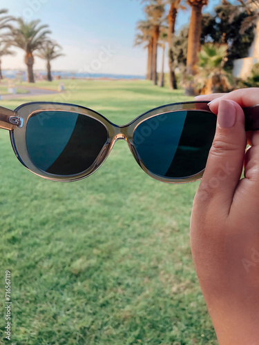 Female hand holding designer sunglasses in hand while enjoying summer vacation on seaside photo