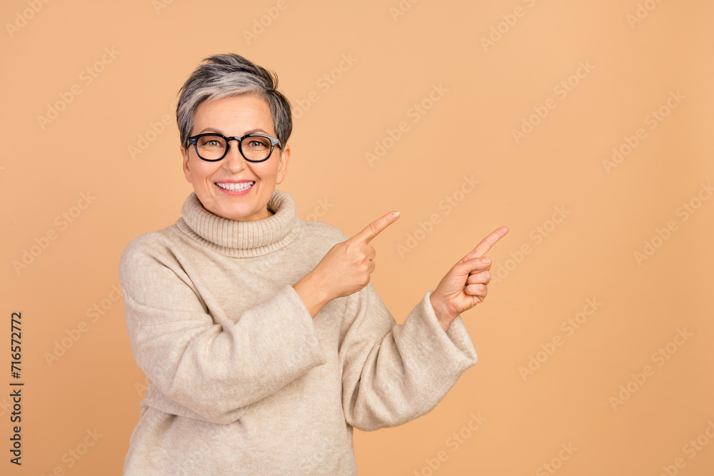 Portrait of friendly grandmother toothy smile indicate fingers empty space ad isolated on beige color background