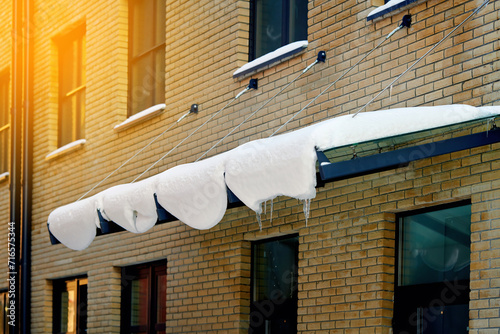Door canopy with melting snow and ice in sunny day, danger for pedestrians. Glass panel mounted with tension rod and wall brackets on building facade. Snow melts on the awning in front of the door photo