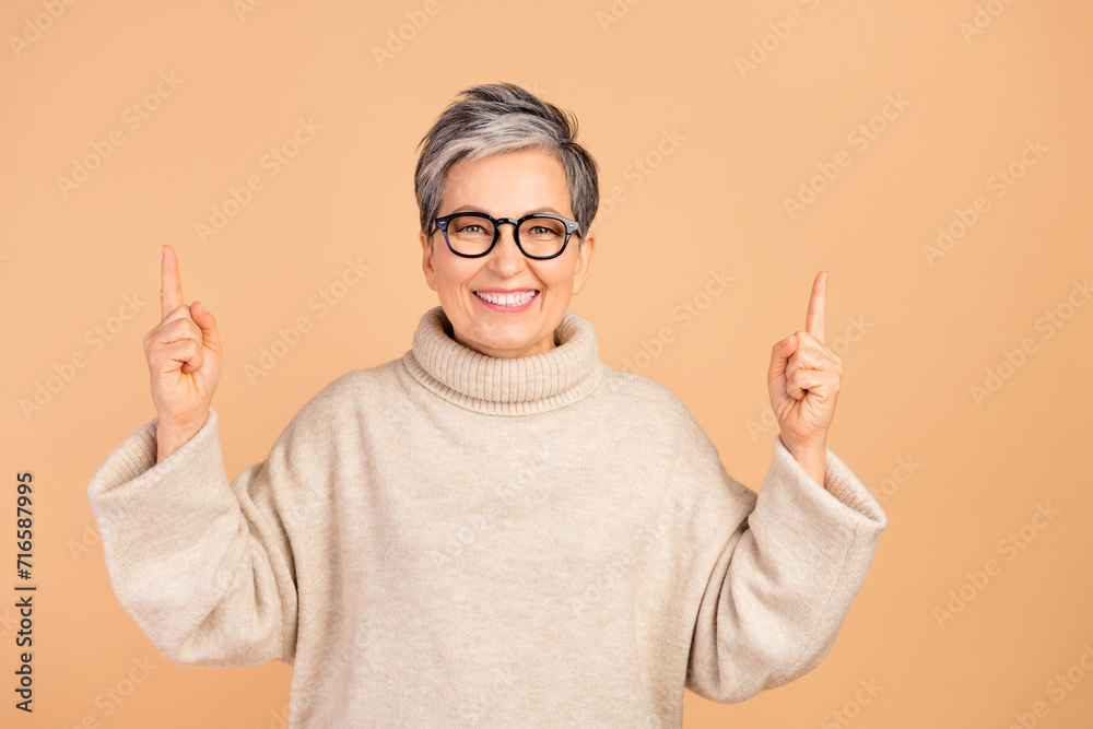 Portrait of charming positive person beaming smile indicate fingers up empty space isolated on beige color background