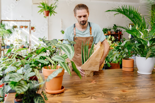 Handsome man wearing apron wrapping a potted plant in paper. Small business entrepreneurs.