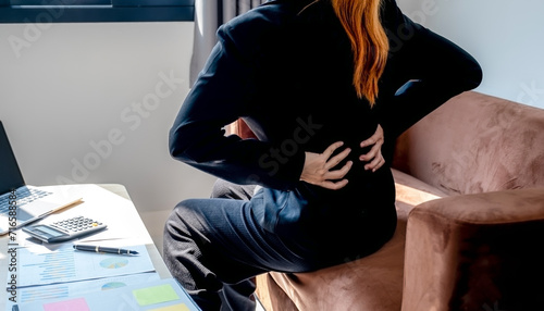 A successful businesswoman feeling waist pain and stretch herself after working hard on computer laptop for a long time in the home office, Office syndrome concept photo