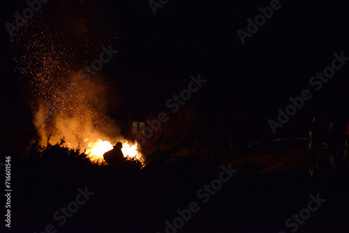 Feuerwehr Mann steht in dunkler Nacht vor Lagerfeuer mit rotem Funkenflug