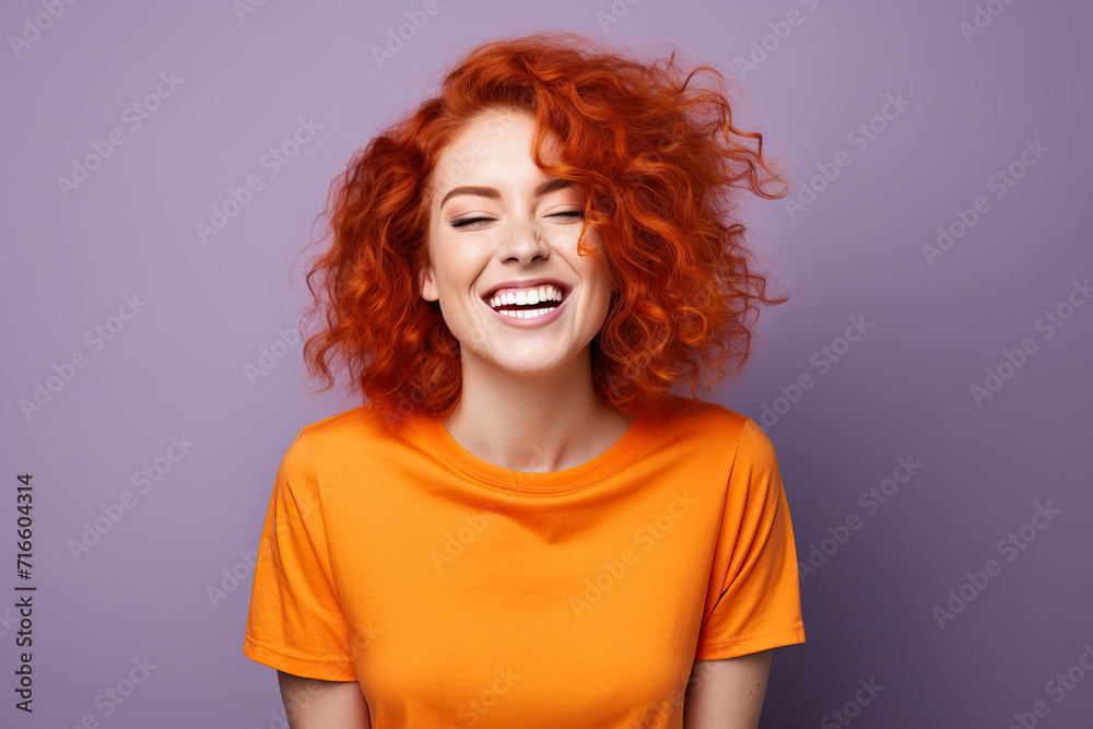 Portrait of young beautiful girl with red curly hair and snow-white smile laughs in T-shirt on bright purple plain background. Human emotions, joy, laughter, happiness Portrait of young beautiful girl with red curly hair and snow-white smile laughs in T-shirt on bright purple plain background. Human emotions, joy, laughter, happiness