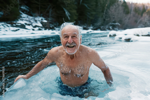 happy elderly gray-haired man bathes in an icy river in winter against the backdrop of a snowy forest © Александр Довянский