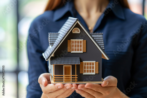A woman holding a miniature house depicting the concept of buying a house, home ownership, or real estate investment