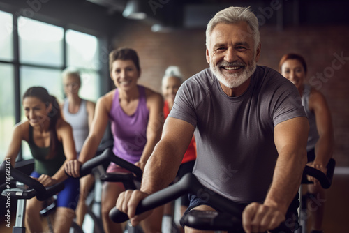 Fit mature man in sportswear doing a cycling class in a gym with a diverse group of people. © FutureStock