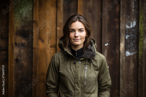 Portrait of a content woman in her 20s dressed in a water-resistant gilet against a rustic wooden wall. AI Generation © CogniLens