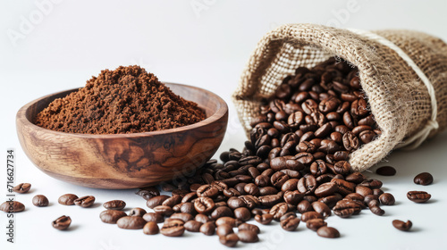 Wooden bowl filled with ground coffee and a burlap sack spilling roasted coffee beans onto a white surface. photo