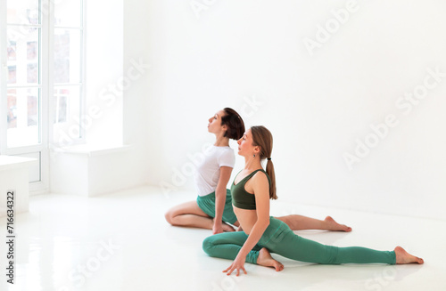 Two young women doing yoga indoor, sitting in position isolated over white studio background