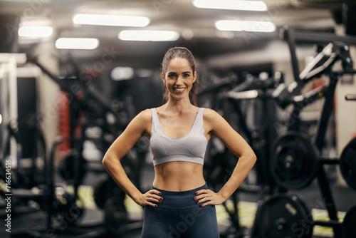 Portrait of a fit sportswoman in shape standing in a gym and smiling at the camera.