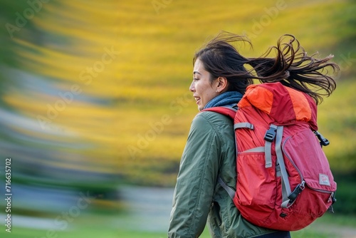 Female hiker with a red backpack in motion, rucking against a blurred yellow background