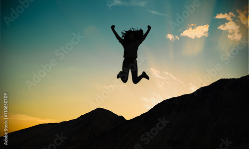 Happy woman silhouette Jumping on mountain against sunset sky. Female joy and adventure 