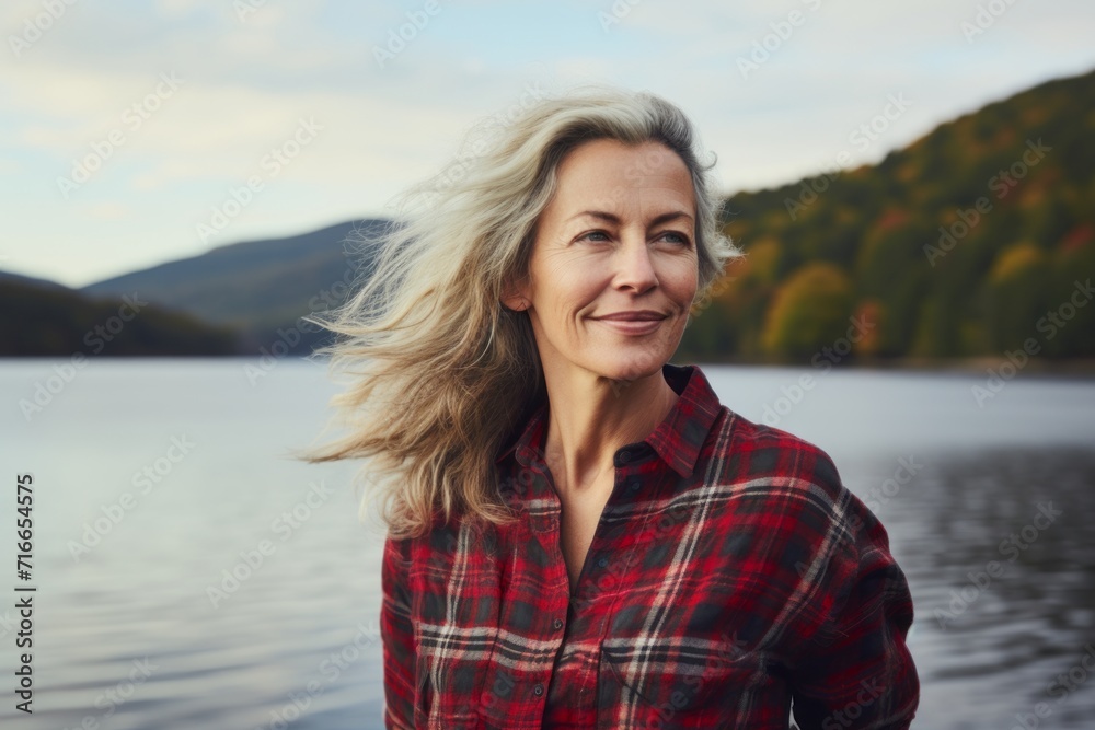 Portrait of a tender woman in her 50s dressed in a relaxed flannel shirt against a serene lakeside view. AI Generation Portrait of a tender woman in her 50s dressed in a relaxed flannel shirt against a serene lakeside view. AI Generation