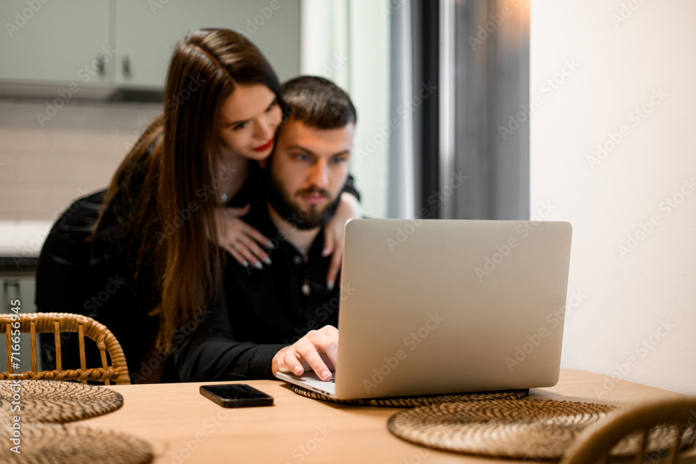 Young woman and a man with are sitting at the table with a laptop Young woman and a man with are sitting at the table with a laptop