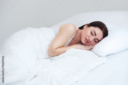 A young woman sleeps on her side in her white bed