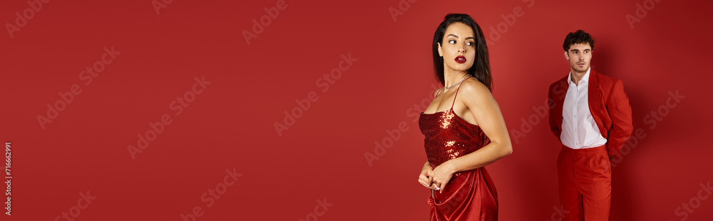 banner of gorgeous and young woman posing in shiny sexy dress near blurred man on red background banner of gorgeous and young woman posing in shiny sexy dress near blurred man on red background