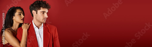 brunette young woman with red lips seducing handsome man in formal wear on red background, banner