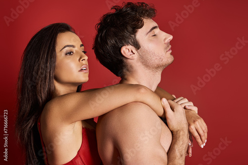 brunette and charming young woman in lace bra embracing her muscular man on red background