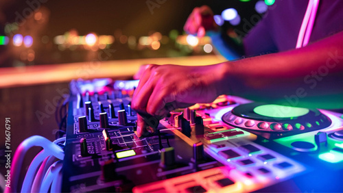 Detalhe da mão de um dj manuseando os botões de um controlador, em uma festa com muitas luzes coloridas.