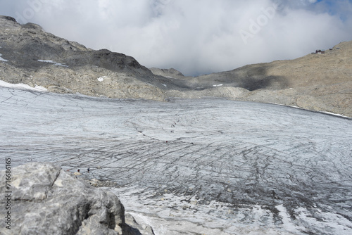 Konstfotografi Hikers traverse a vast glacier under a cloud-covered sky