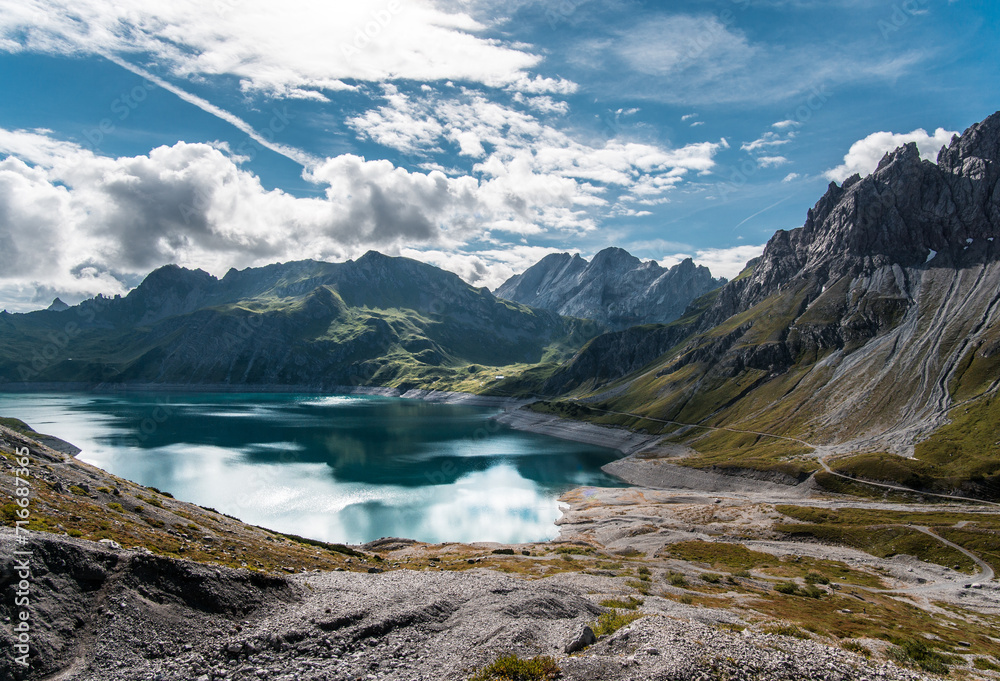 A tranquil mountain lake nestled among rugged peaks under a partly cloudy sky.