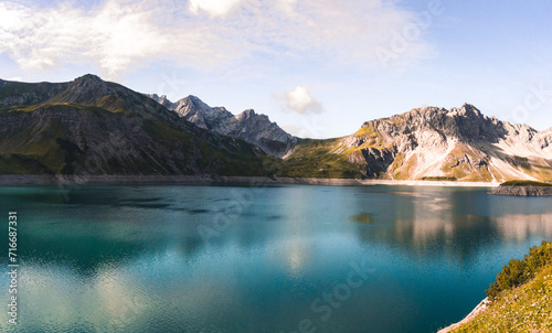 Panoramic view of a tranquil mountain lake with clear blue waters and surrounding peaks.