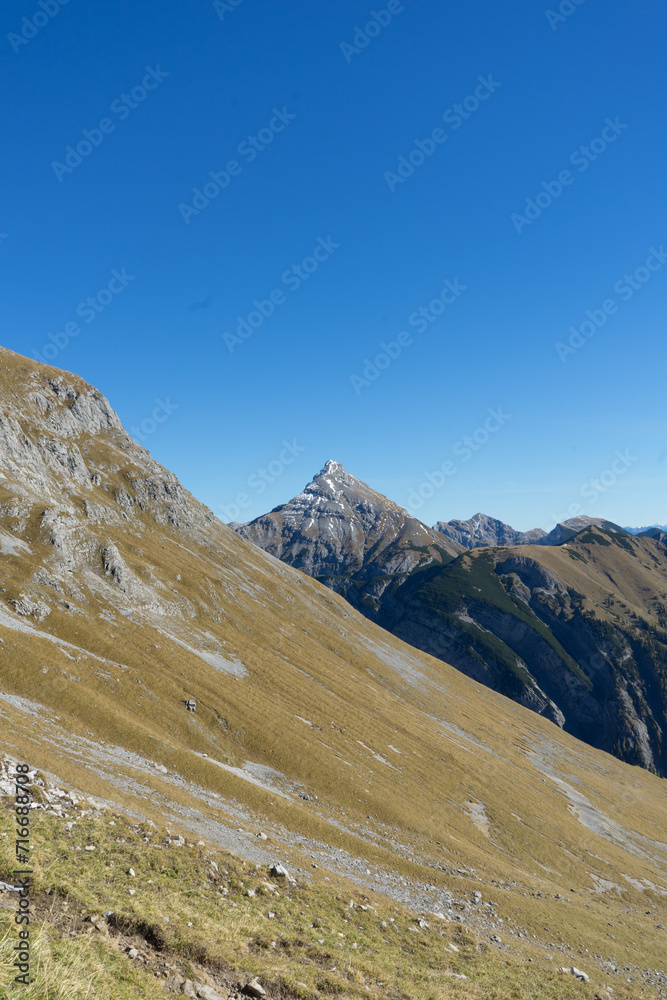 A majestic mountain peak rising above rolling green hills under a clear blue sky.