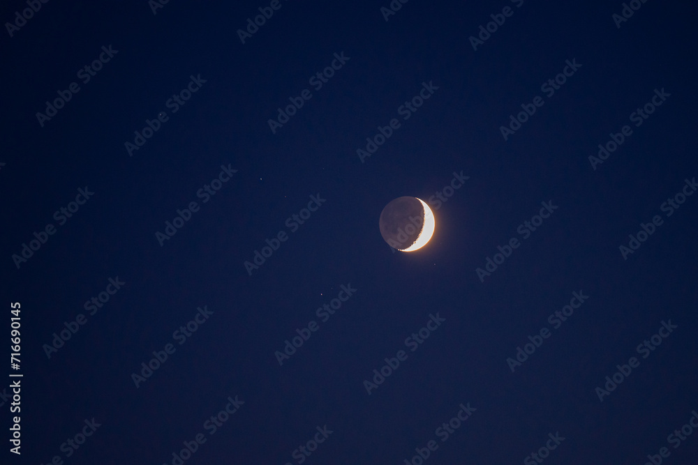 Natural satellite of the earth. Young crescent moon on a clear sky at the end of the day in the summer Natural satellite of the earth. Young crescent moon on a clear sky at the end of the day in the summer