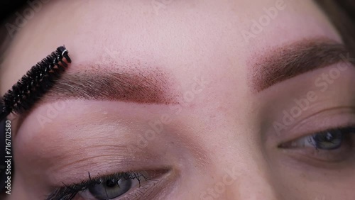 Close-up of eyebrows on which permanent eyebrow makeup is performed, combing eyebrow hairs with a brush. Permanent makeup procedure, performing PMU of eyebrows photo