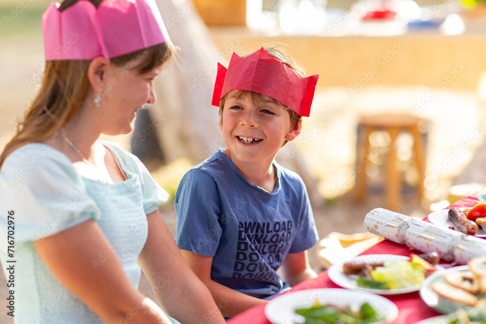 school-aged brother and sister wearing paper crowns sitting at a table for Christmas lunch school-aged brother and sister wearing paper crowns sitting at a table for Christmas lunch